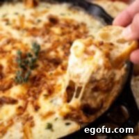 Close up looking at a hand dipping a cracker in Hot French Onion Dip.