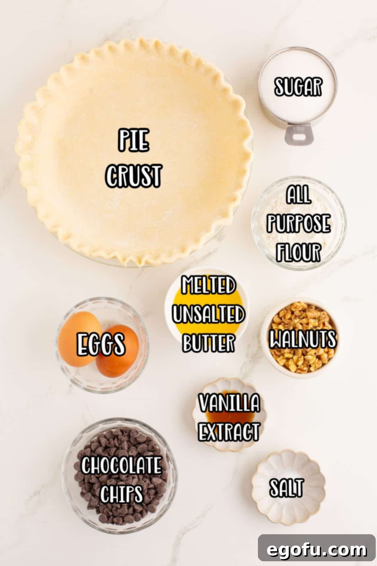 A clear display of all the key ingredients for Kentucky Derby Pie: unbaked pie crust, unsalted butter, granulated sugar, large eggs, vanilla extract, all-purpose flour, chopped walnuts, and semi-sweet chocolate chips.