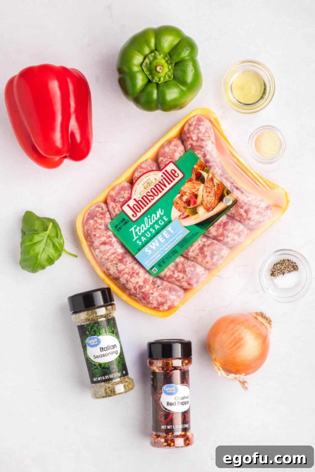 One Pan Sausage and Pepper Bake 4 Sausage links, green bell peppers, red bell pepper, onion, crushed red pepper, olive oil, Italian seasoning, salt, pepper, and basil arranged as ingredients.