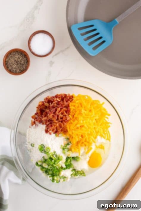 Crispy Potato Fritters 10 A bowl with potatoes, flour mixture, cheese, bacon, green onion, and egg.