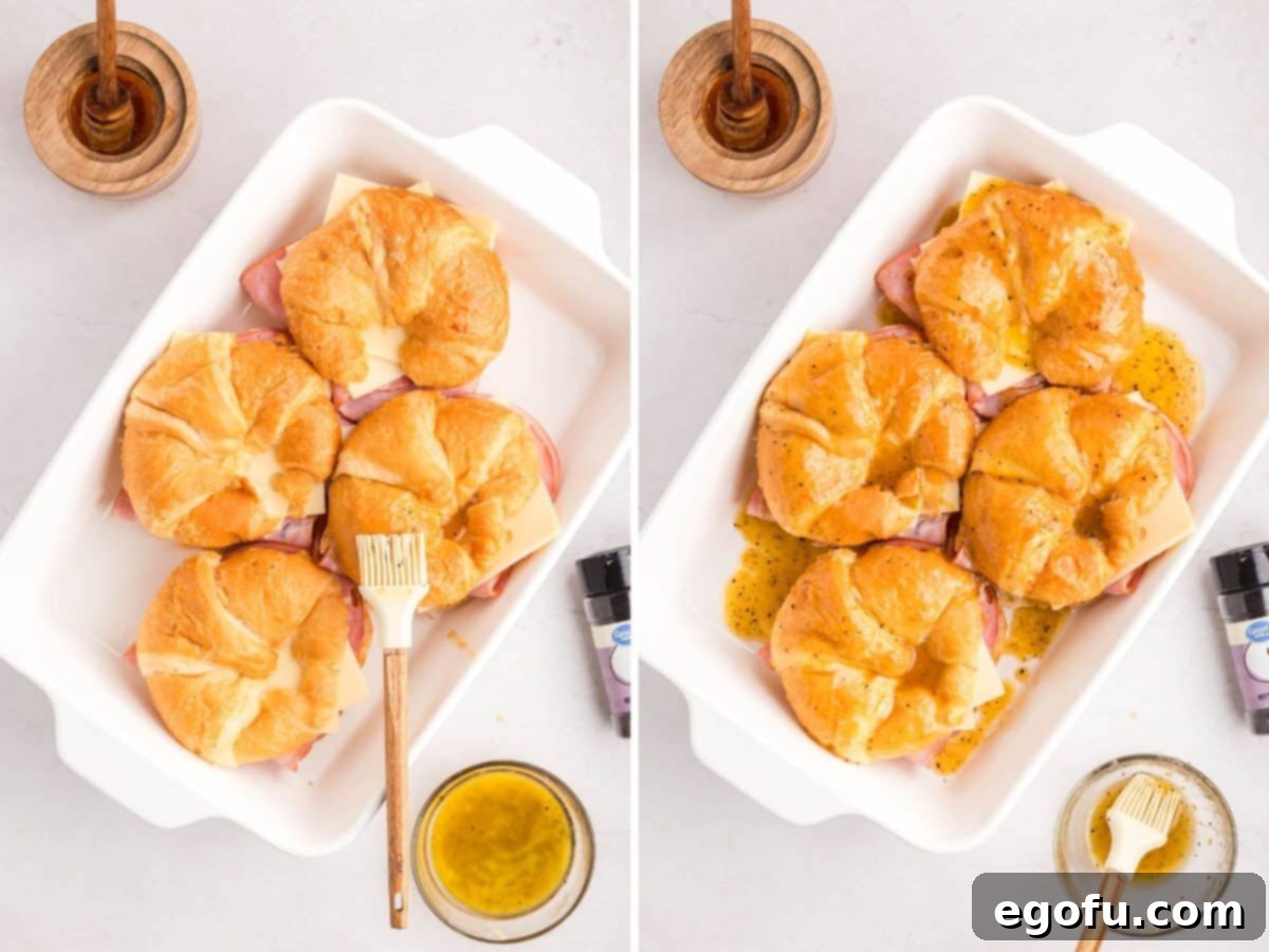 A pastry brush brushing the butter sauce on the croissant tops and then baked sandwiches in a baking dish.