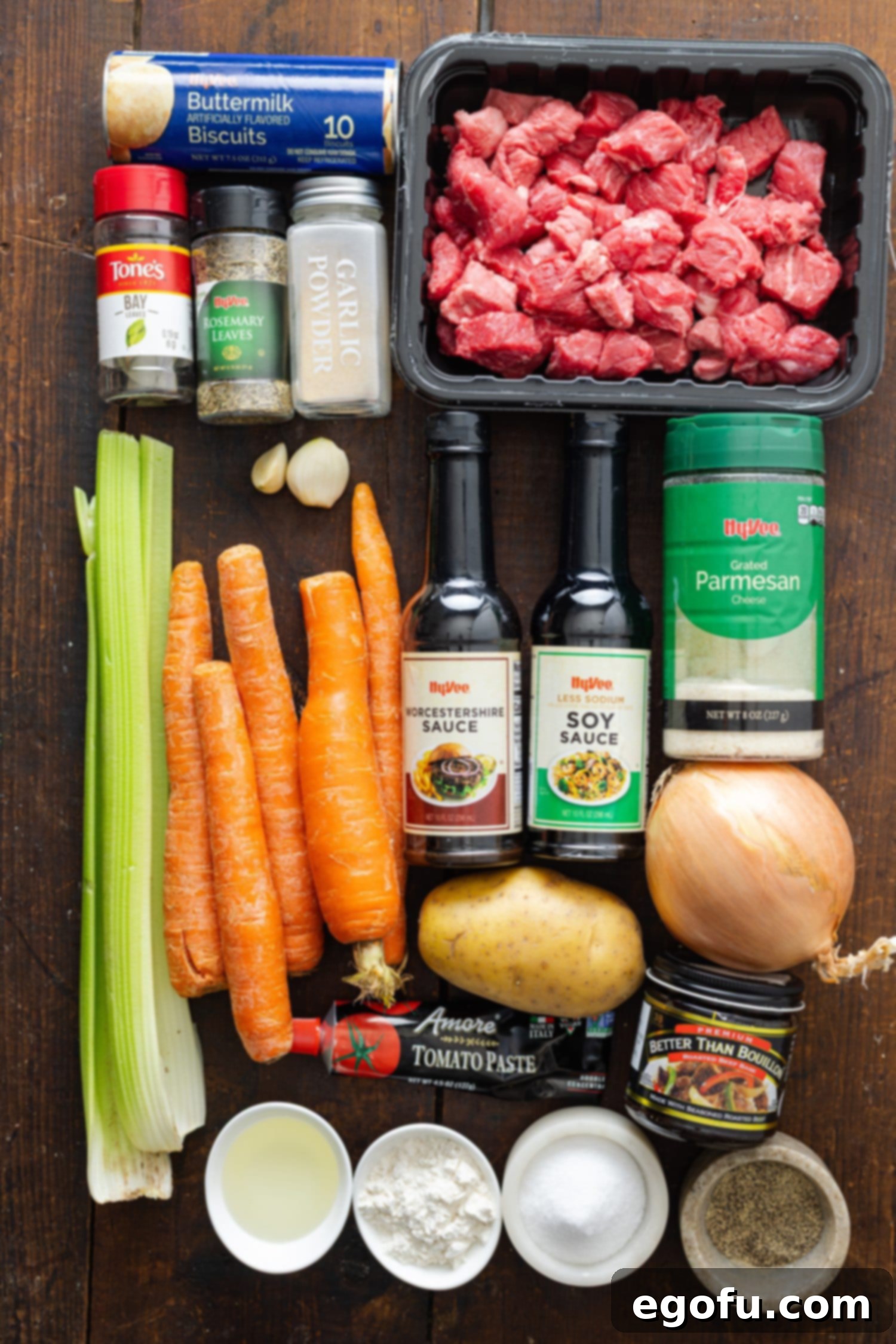 A flat lay of all the ingredients for Crock Pot Beef Dumplings, including beef stew meat, fresh vegetables, broth, seasonings, and canned biscuits.