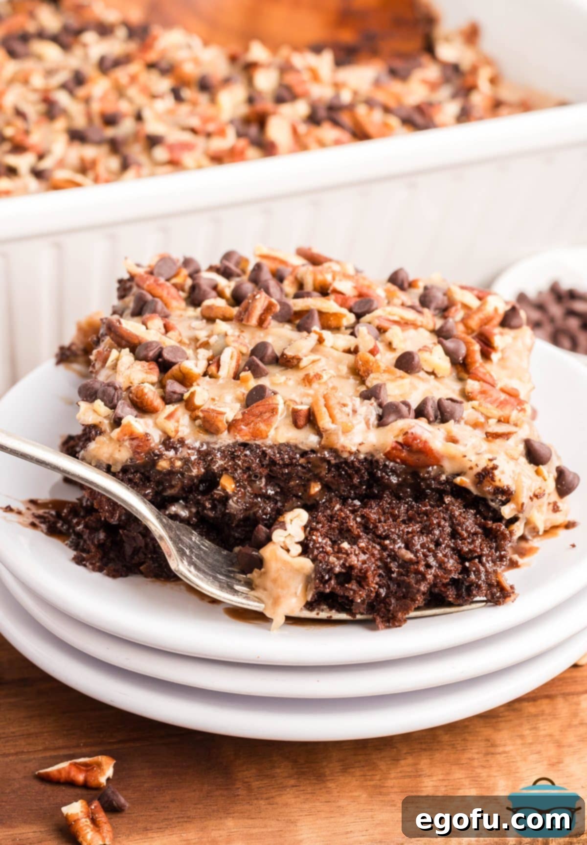 A fork holding a perfect bite of German Chocolate Poke Cake on a white plate, highlighting the moist cake and rich frosting.