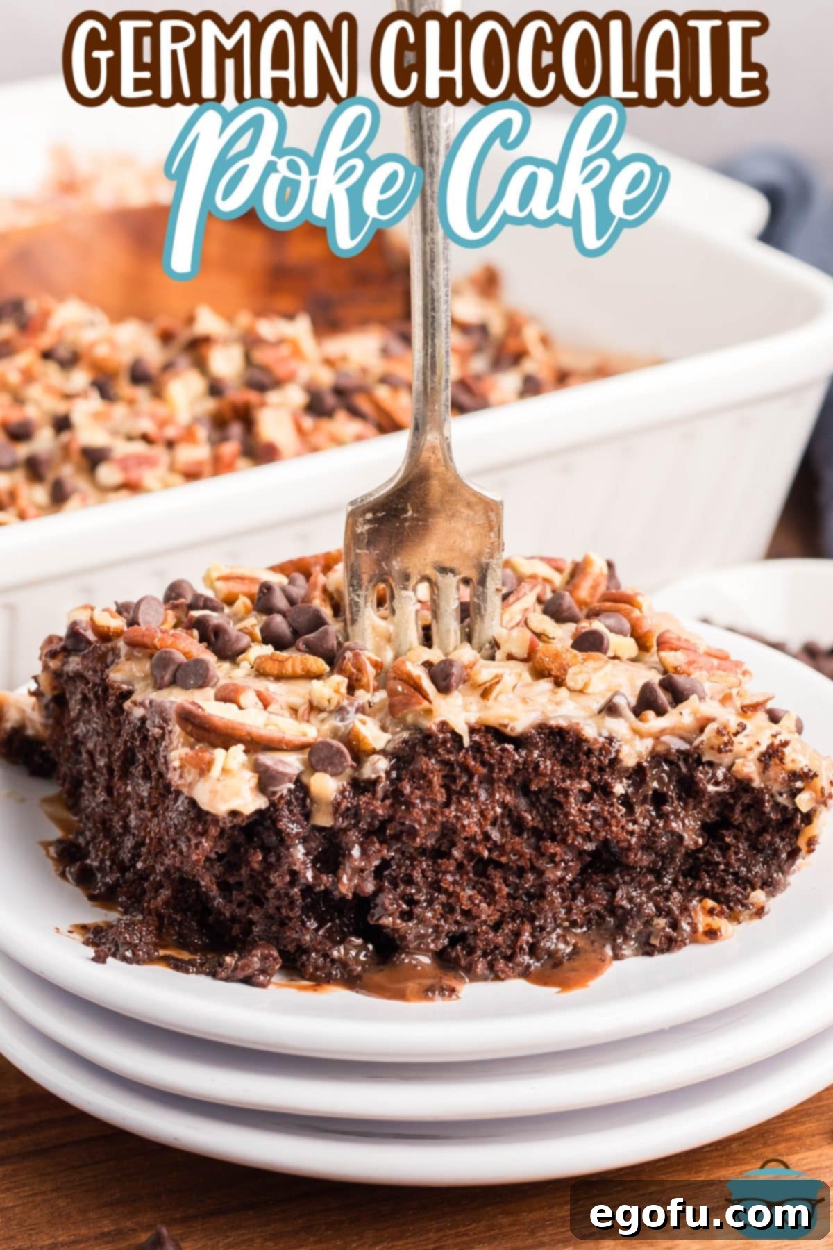 A fork standing upright in a generous slice of German Chocolate Poke Cake, showcasing its moist texture and rich frosting.