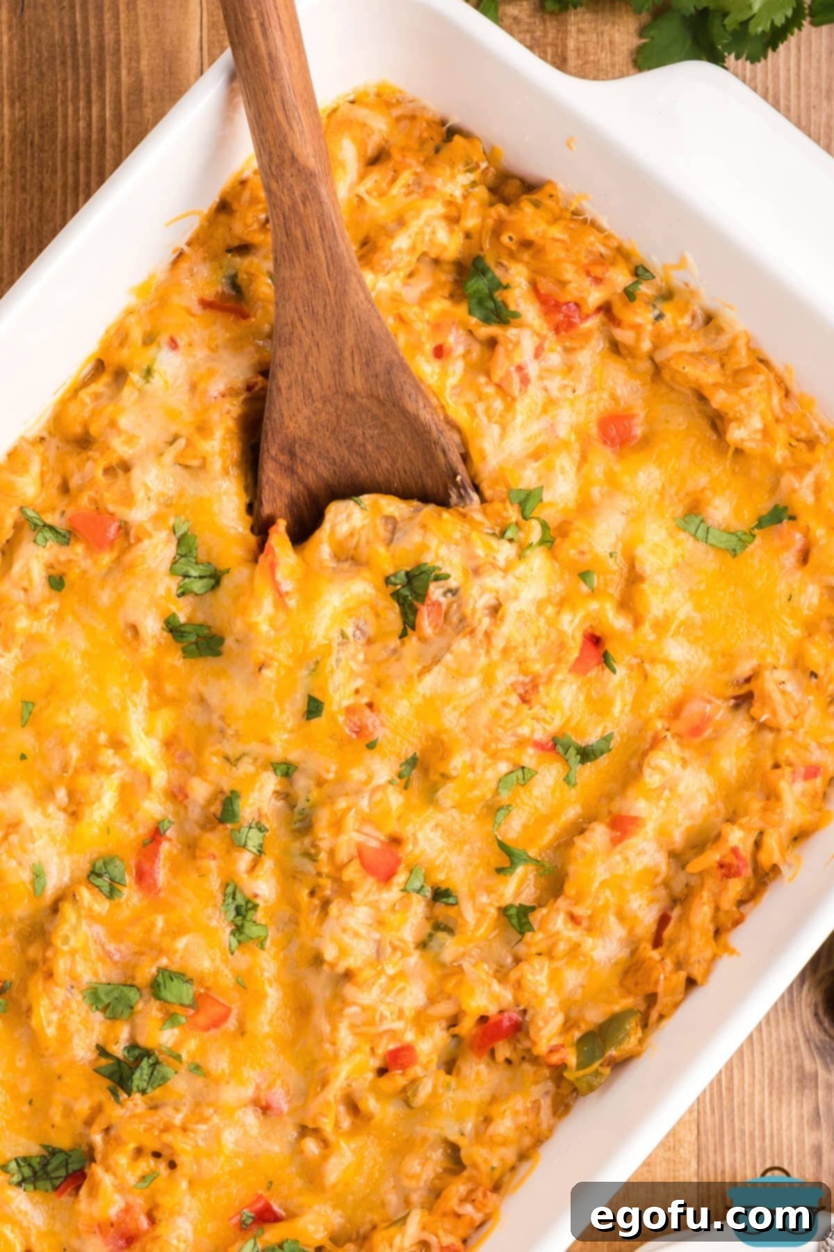 Looking down on a full Chicken Fajita Casserole in a baking dish with a wooden spoon getting ready to scoop some out.
