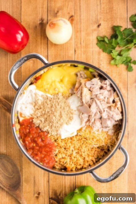 A pan with peppers, onions, chicken, rice, soup, salsa, cream cheese, 1/2 of the cheese, sour cream, and fajita seasoning.