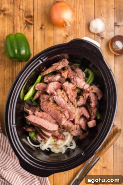 A crockpot with all the uncooked ingredients for cheesesteaks.