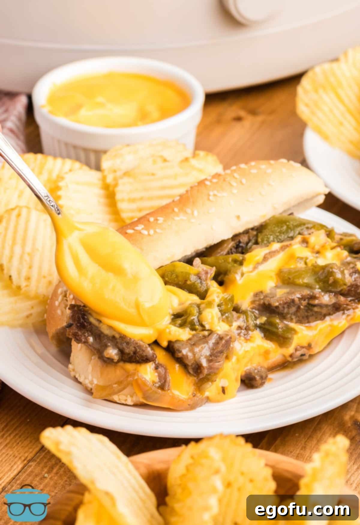 A spoon with Cheez Whiz being drizzled on Crock Pot Philly Cheesesteaks.