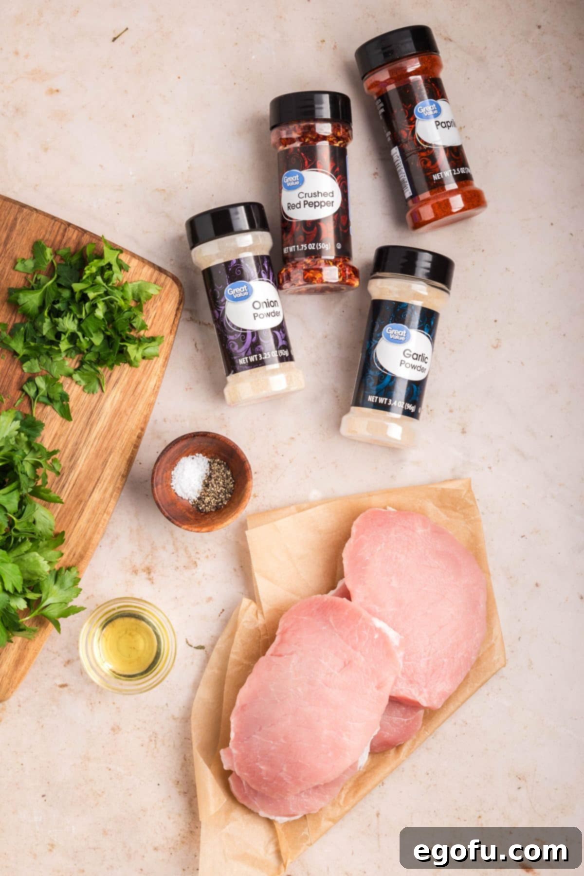 Pork chops, oil, paprika, garlic powder, onion powder, salt, pepper, red pepper flakes, and parsley arranged for the recipe.
