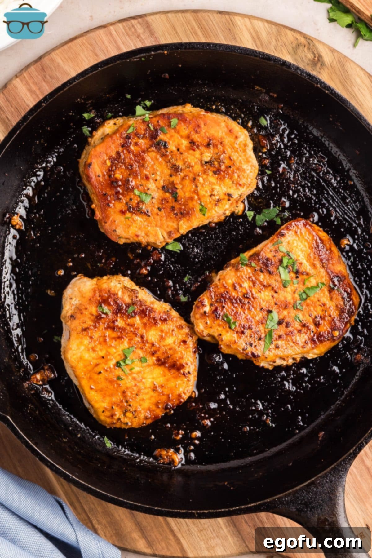 A skillet containing three beautifully cooked pork chops, garnished with parsley.
