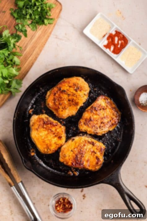 Pork chops cooking in a black cast iron skillet.