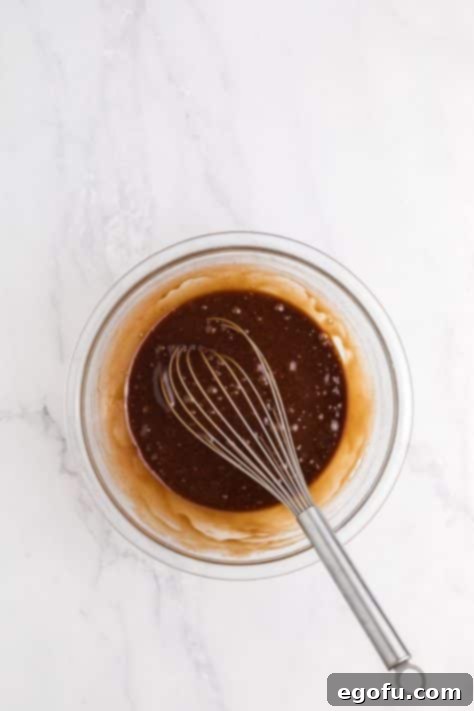 A whisk blending eggs, sugar, and vanilla into the chocolate mixture for brownie batter.