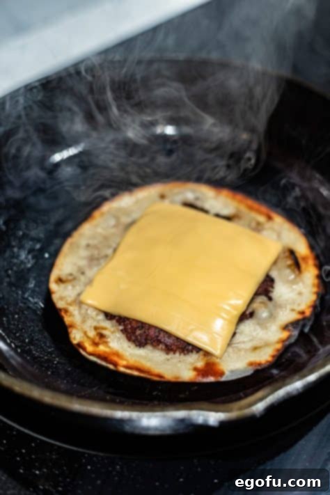 MacSmash Taco 15 Cheese on top of a Smashburger on a tortilla melting in a skillet.