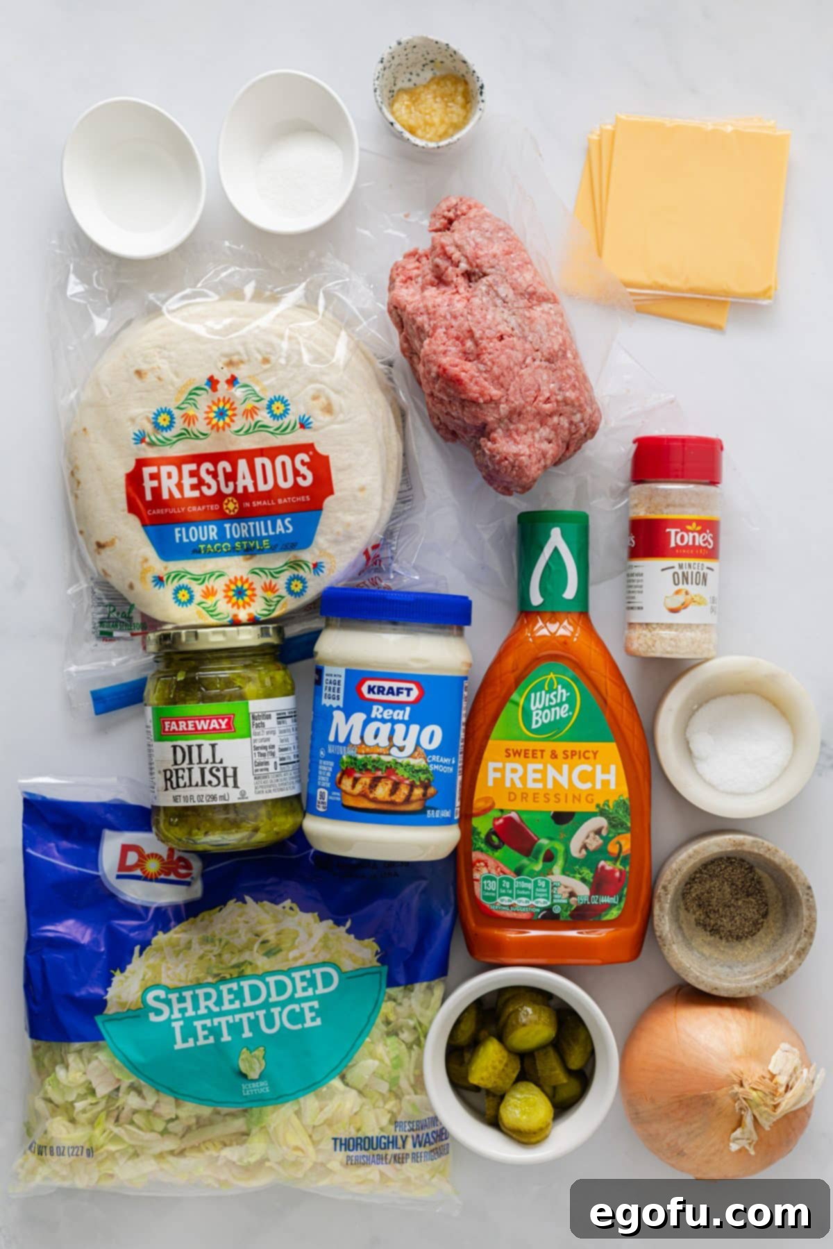 MacSmash Taco 4 A vibrant flat lay of all the essential ingredients for Big Mac Smashburger Tacos: tortillas, ground beef, American cheese, fresh onion, shredded lettuce, pickles, salt, pepper, mayonnaise, French dressing, dill pickle relish, dried minced onion, granulated sugar, white vinegar, and minced garlic.