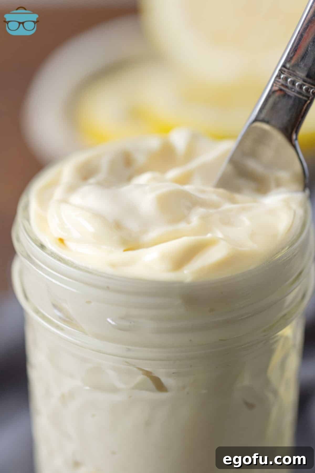 A knife dipping into a clear mason jar filled with freshly made, rich, and creamy homemade mayonnaise, highlighting its smooth texture and appetizing appearance.