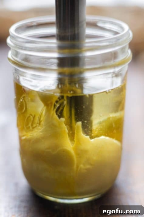 Homemade Mayonnaise is being expertly mixed in a jar using an immersion blender, illustrating the perfect technique for achieving a smooth and creamy texture.