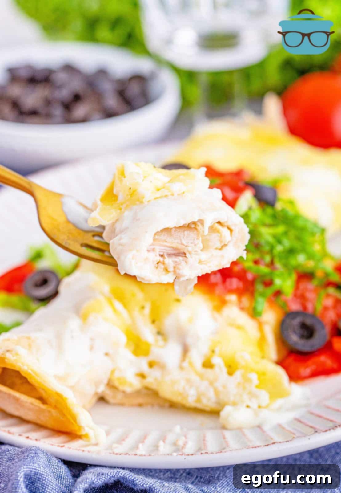 A fork holding up a slice of Swiss enchiladas over a plate with two enchiladas on the plate, showcasing the creamy texture and golden-brown cheese topping.