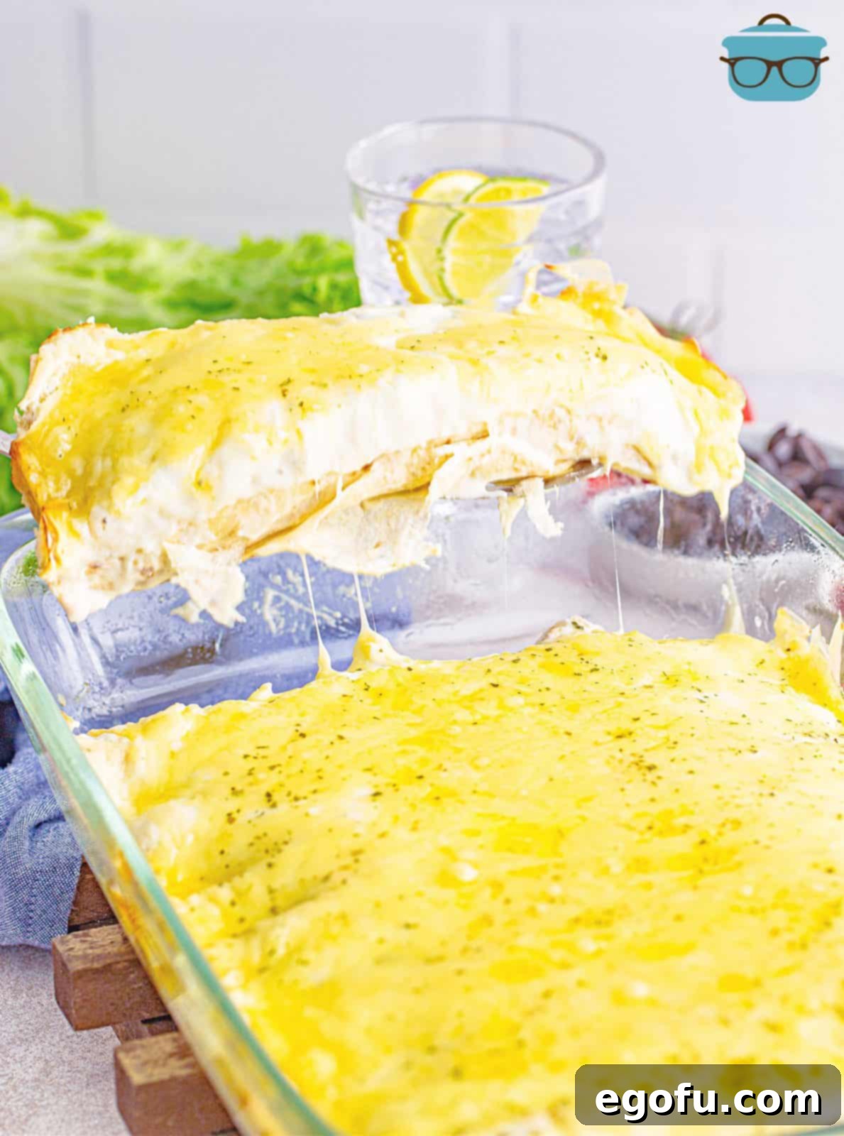 A fully baked dish of Swiss enchiladas, golden and bubbling, with a spatula gently scooping out two servings from the dish.