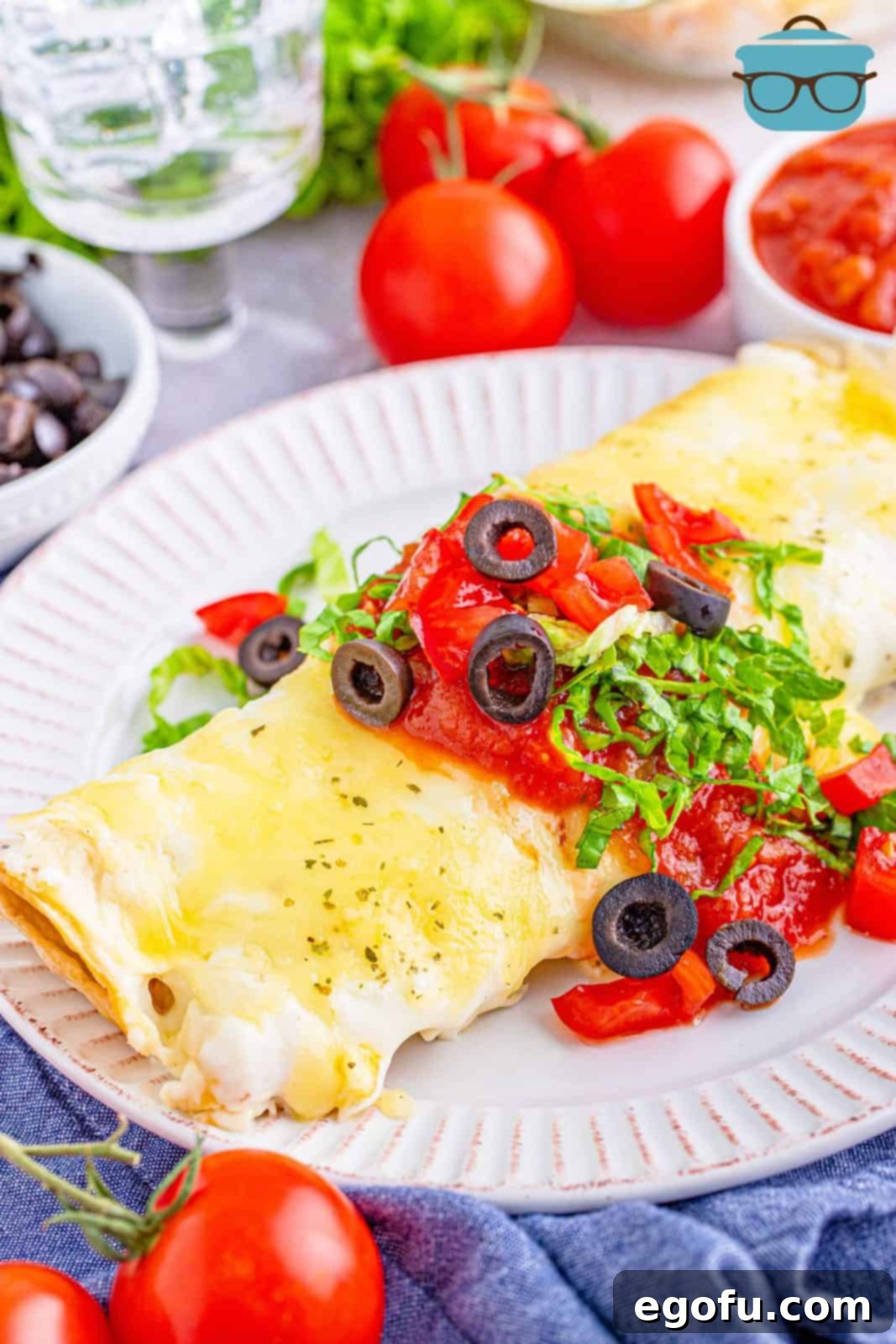 Two perfectly cooked Swiss Enchiladas presented on a white plate, artfully topped with fresh salsa, black olives, and shredded lettuce, ready to be enjoyed.