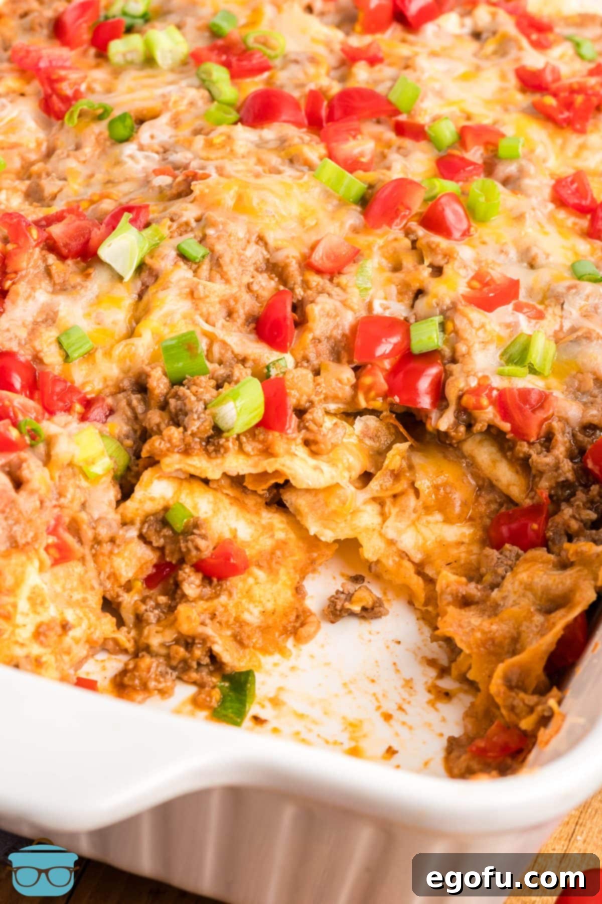 A casserole dish with a scoop missing from a delicious Taco Bell Mexican Pizza Casserole, showing the layers of ingredients.