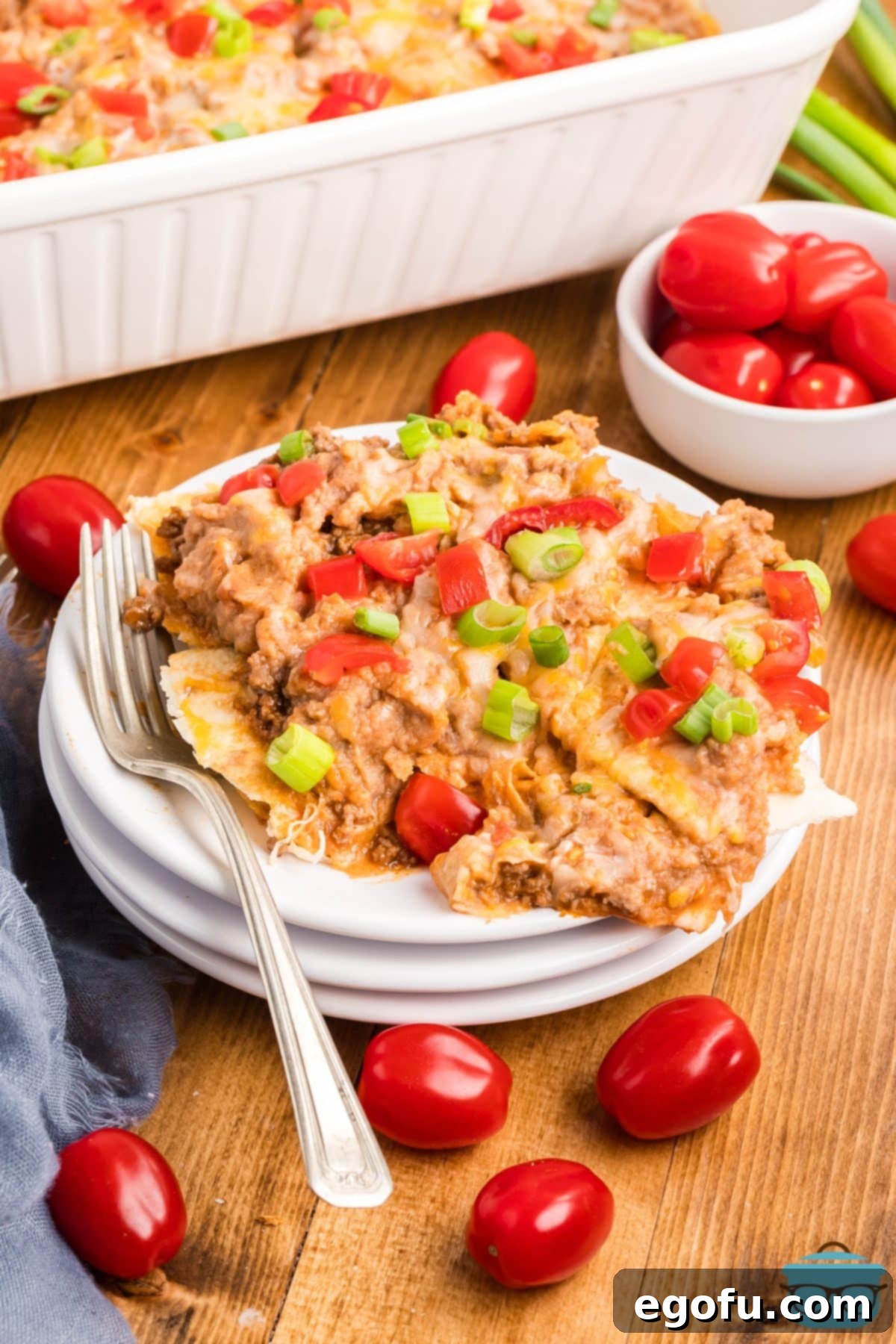 A stack of plates with one plate full of a generous serving of Taco Bell Mexican Pizza Casserole, accompanied by a fork.