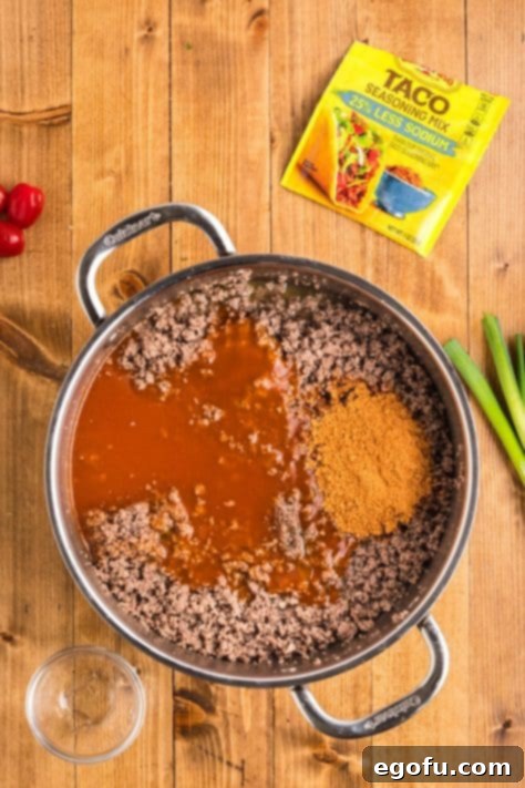Ground beef mixed with taco seasoning and enchilada sauce, simmering in a skillet.