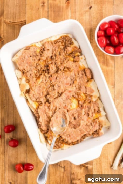 The creamy refried bean layer spread over the meat and tortillas in the baking dish.