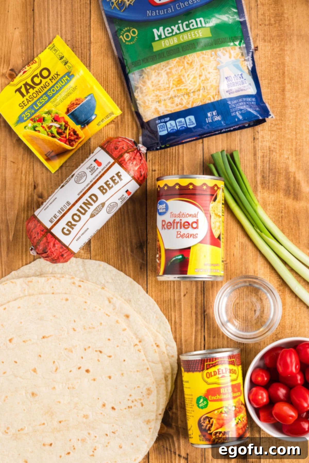 An array of ingredients for Taco Bell Mexican Pizza Casserole: tortillas, refried beans, enchilada sauce, taco seasoning, water, cheese, diced tomatoes, and green onions.