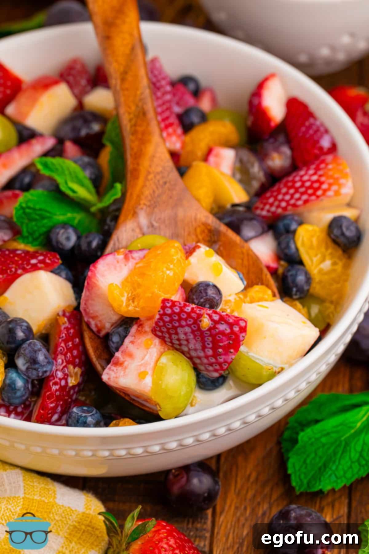 Looking down on a serving bowl with a wooden spoon in a Creamy Fruit Salad.