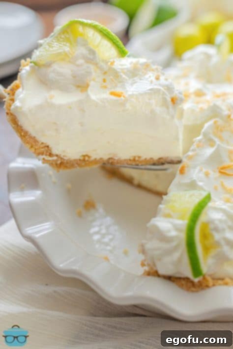 A slice of Key Lime Cream Pie being removed from the rest of the pie, garnished with lime and whipped cream.