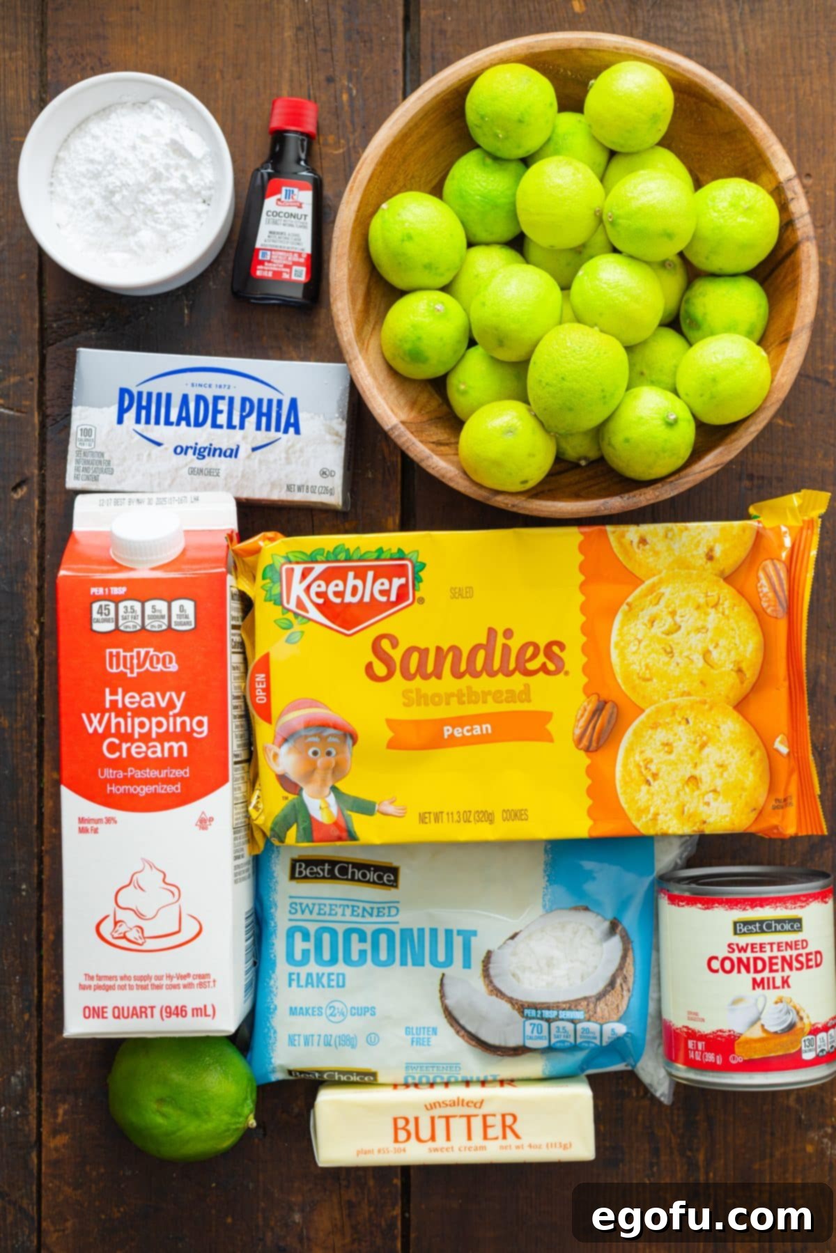 A flat lay of all the Key Lime Cream Pie ingredients: Pecan Sandie Cookies, key limes, heavy whipping cream, cream cheese, coconut extract, sweetened condensed milk, butter, powdered sugar, and coconut flakes.