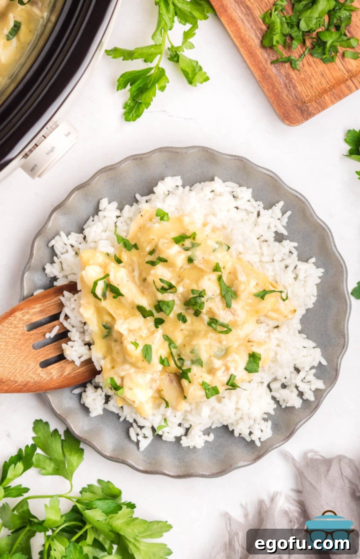 Creamy Ranch Slow Cooker Chicken 8 A wooden serving utensil adding a generous serving of creamy Chicken and Ranch on top of a bed of white rice on a plate, garnished with fresh parsley.