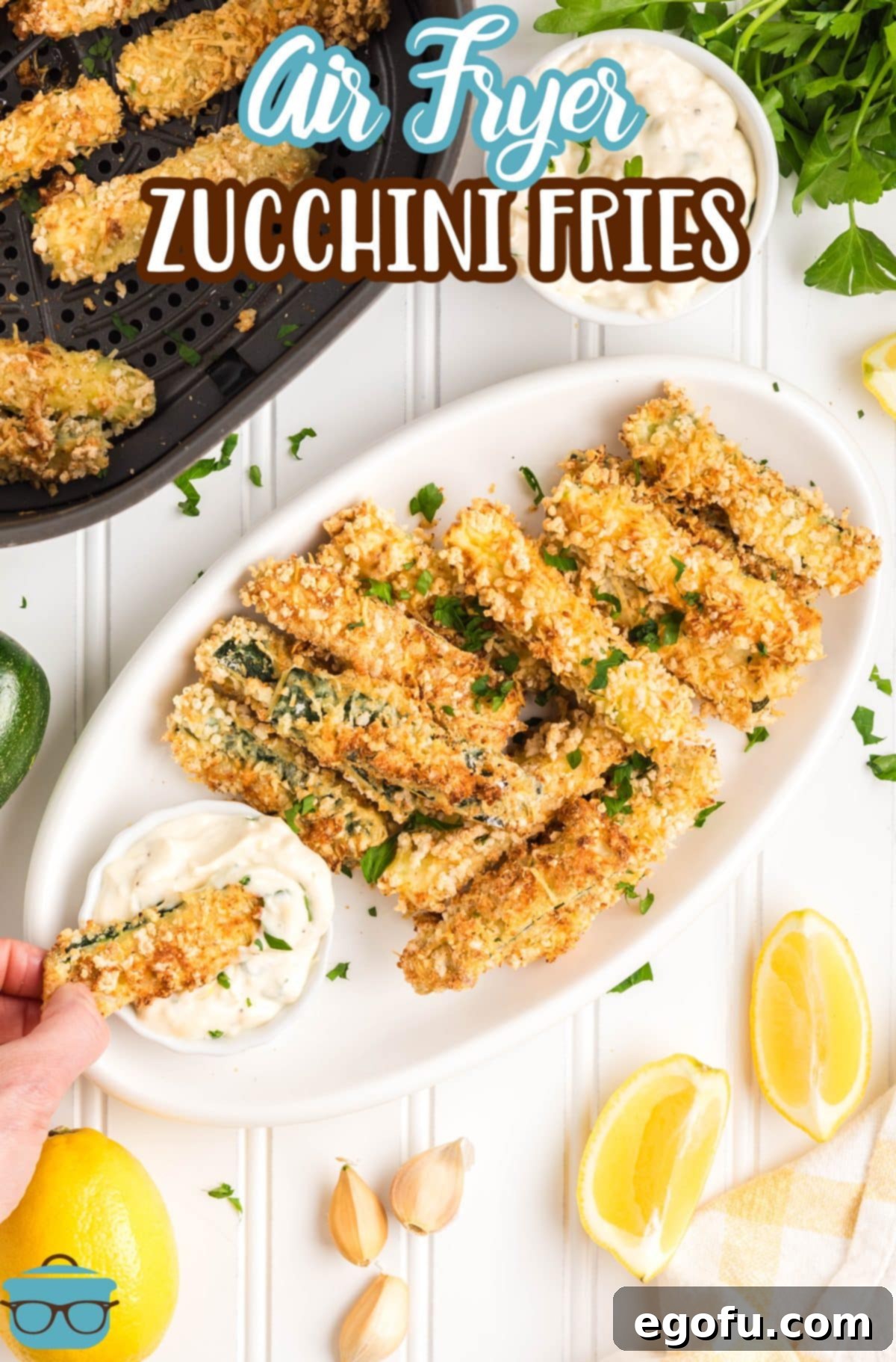 A hand dipping an Air Fryer Zucchini Fries in sauce next to a pile of the rest of them.