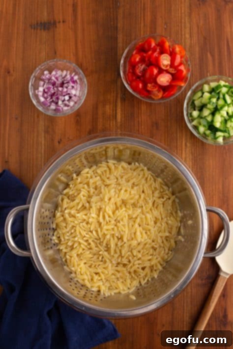 Orzo pasta cooling in a colander after cooking.