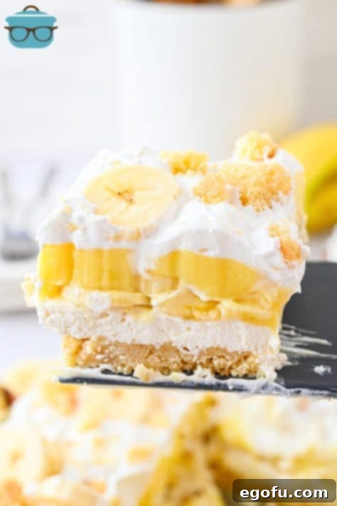 A slice of Banana Pudding Layered Dessert being held above the baking dish.