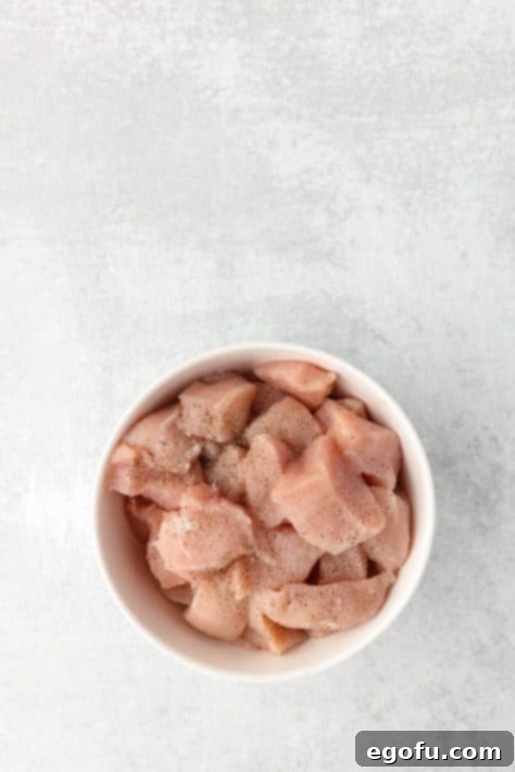 Diced chicken breast pieces seasoned with salt and pepper, ready for cooking.