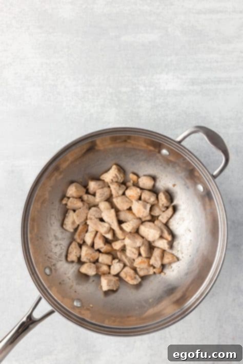 Seasoned chicken cooking in a skillet to a golden brown.