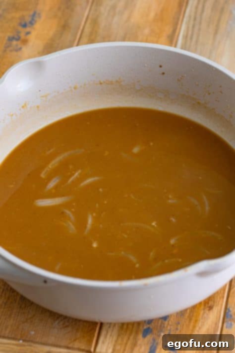 Tender Pork Bites in Rich Gravy 14 Beef stock being slowly incorporated into the roux, creating a smooth gravy base.