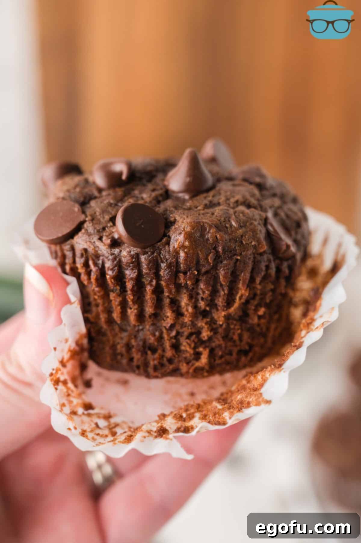 Secretly Healthy Chocolate Zucchini Muffins 2 A hand removing a muffin wrapper of a Chocolate Zucchini Muffin.