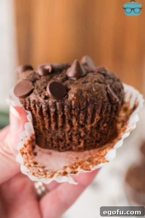 Secretly Healthy Chocolate Zucchini Muffins 13 A hand removing a muffin wrapper of a Chocolate Zucchini Muffin.