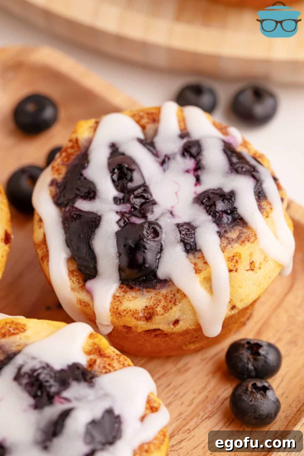 Blueberry Cinnamon Swirl Bites 6 A close-up shot of a single, perfectly baked Blueberry Cinnamon Roll Cup, showcasing its sweet, gooey blueberry filling and luscious glazed top.