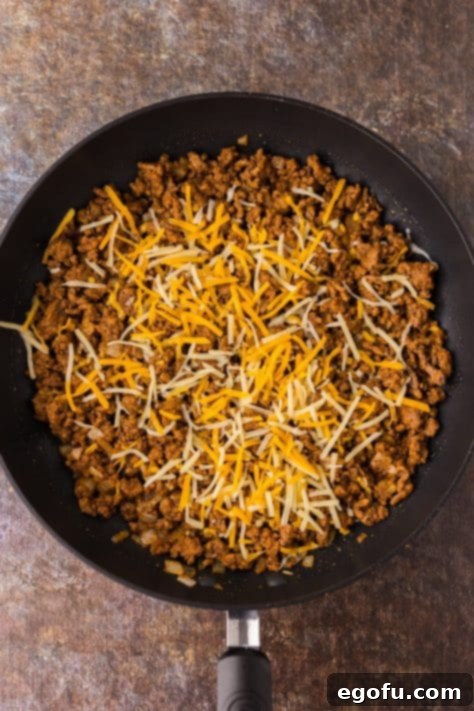 Shredded cheese melting into taco seasoned ground beef in a skillet.
