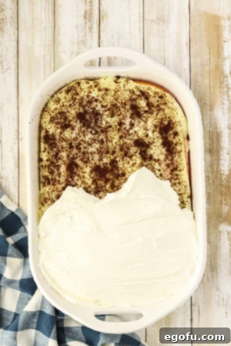 Espresso Kissed Tiramisu Poke Delight 17 Whipped topping being spread over a dessert.