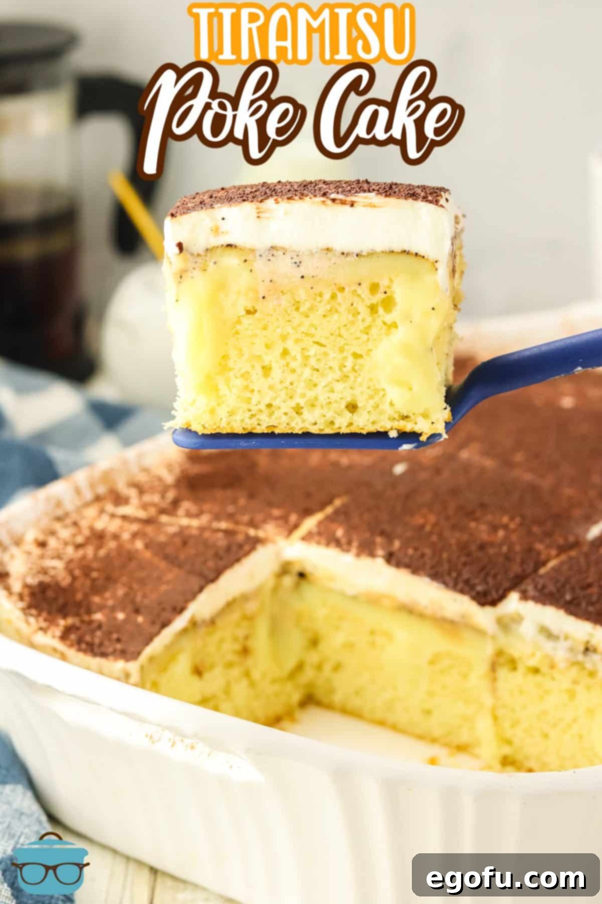 Espresso Kissed Tiramisu Poke Delight 5 A serving utensil holding a slice of Tiramisu Poke Cake above the rest of the cake in the cake dish.