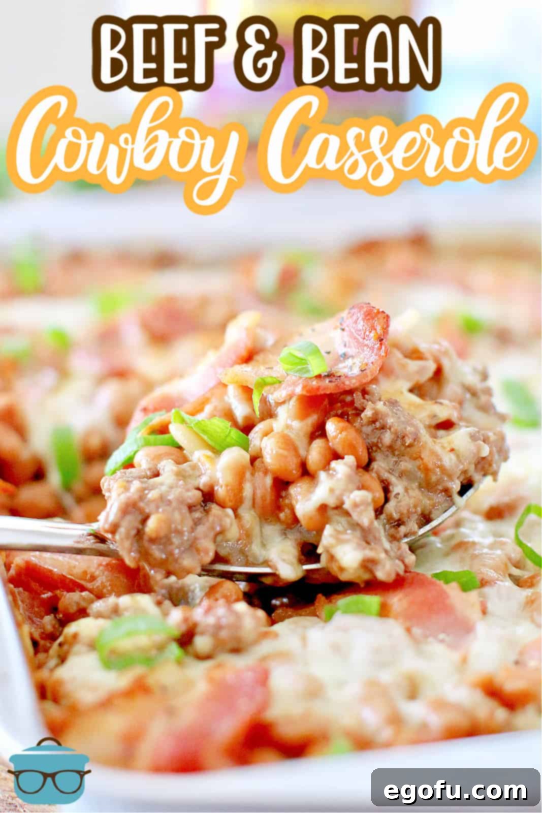 A large serving spoon scooping a portion of Beef and Bean Cowboy Casserole from a white baking dish, showcasing the layers of beef, beans, bacon, and melted cheese.