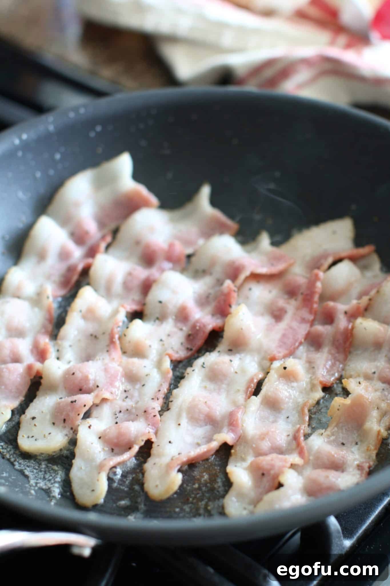 Slices of bacon partially cooking in a hot skillet, becoming golden and ready to be transferred.