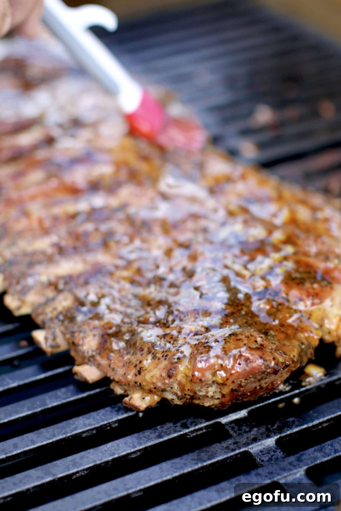 pastry brush rubbing on orange marmalade on rack of ribs on the gas grill.