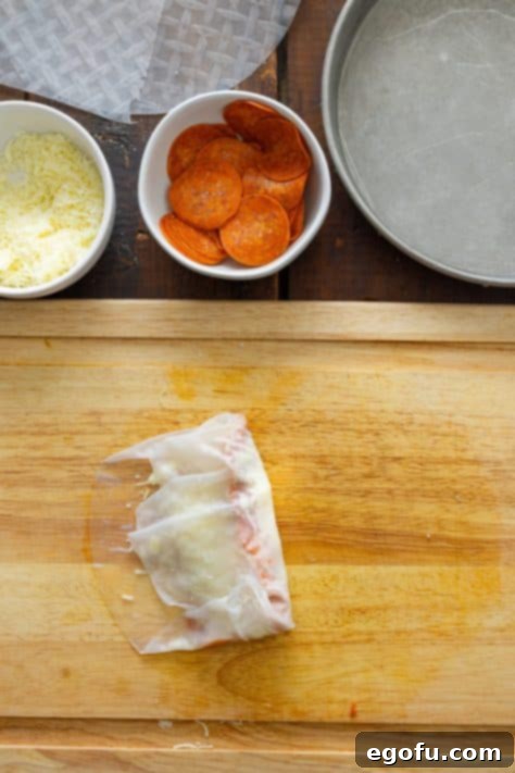 A pepperoni roll being wrapped in a spring roll wrapper.