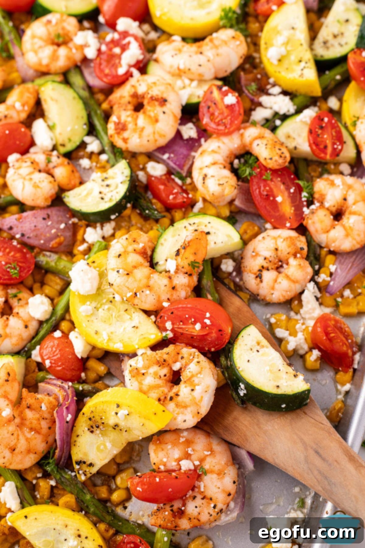 Looking closer down on a Sheet Pan Shrimp and Vegetables with a wooden spoon grabbing some.