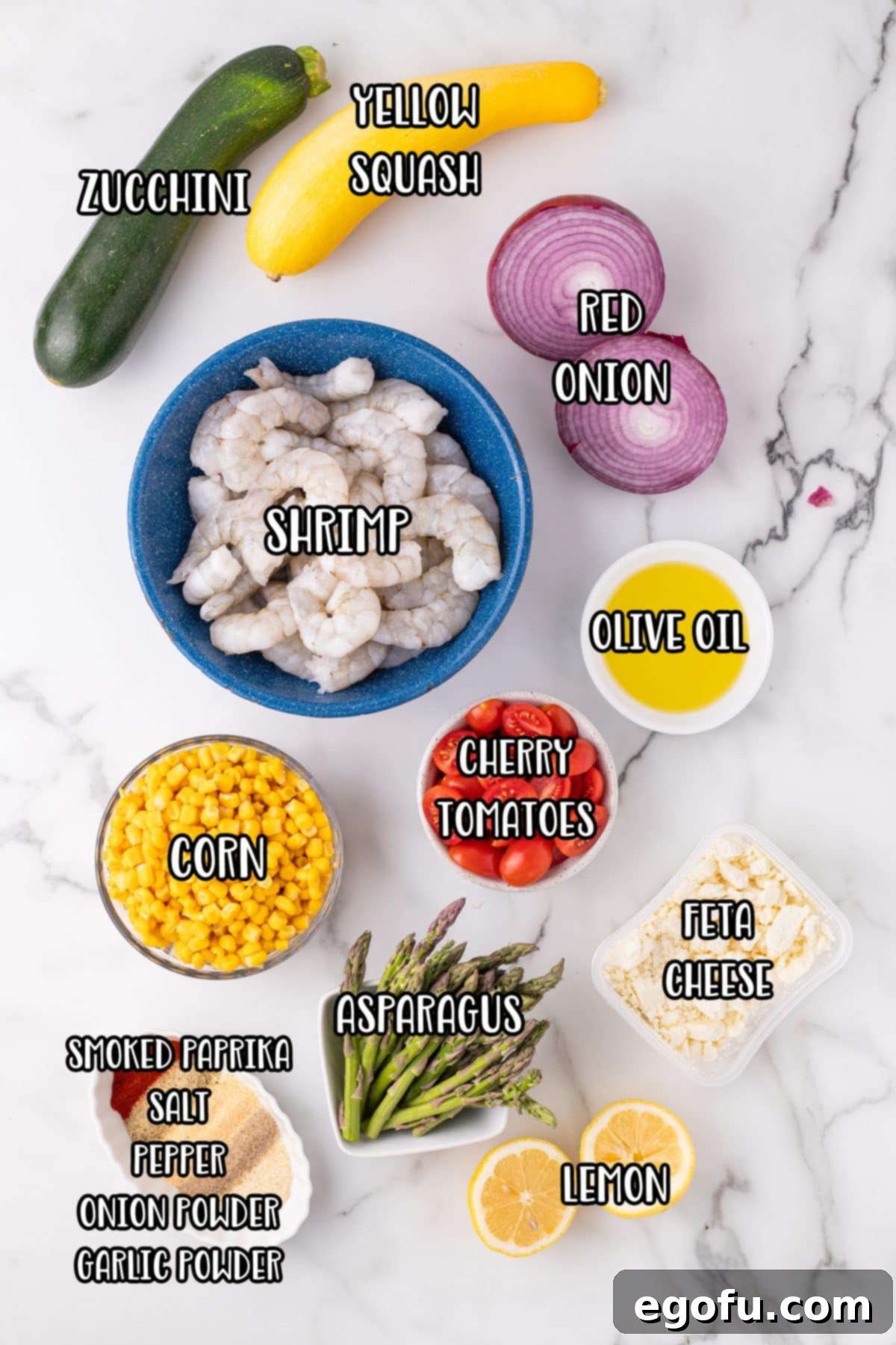 Shrimp, zucchini, yellow squash, red onion, olive oil, tomatoes, corn, asparagus, lemon, feta cheese, smoked paprika, salt, and pepper laid out as ingredients.